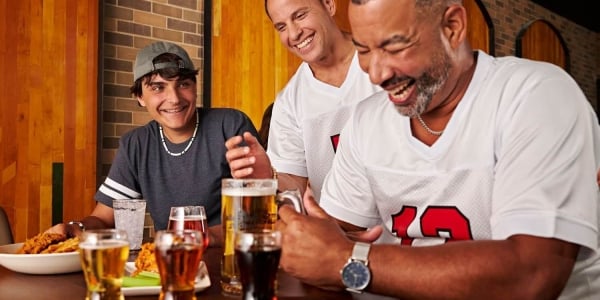 three men laughing and enjoying drinks and food while wearing football jerseys