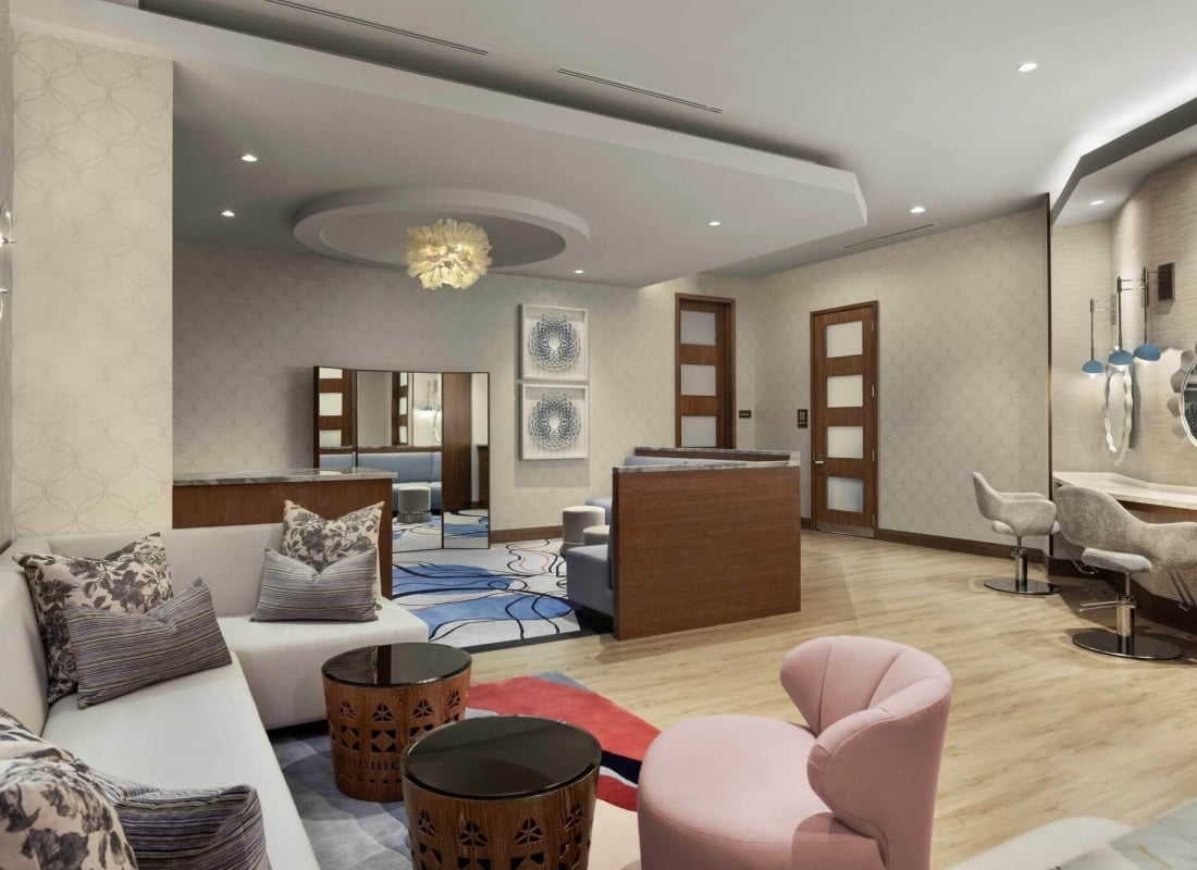 Bridal Suite lounge with wooden tables, a white couch, a pink chair, and a bar with two salon chairs