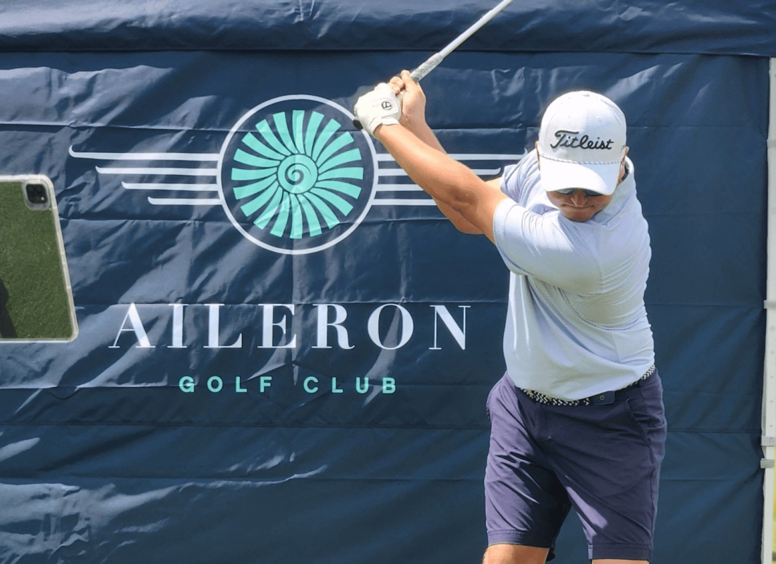 Golfer teeing off with Aileron Golf Club signage behind him