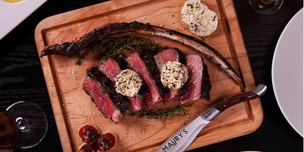 Steak slices with butter on wooden board with knife, herbs, and cherry tomatoes at Maury's