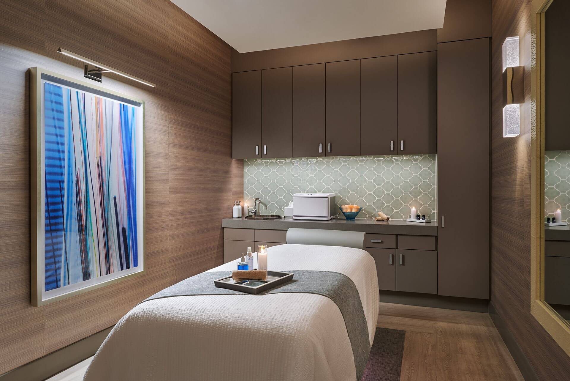Massage room with a treatment bed, cabinets, and a colorful abstract painting on the wall