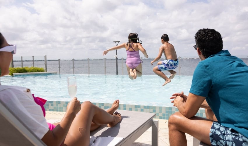 Kids jumping in the pool as parents watch over from sunbeds
