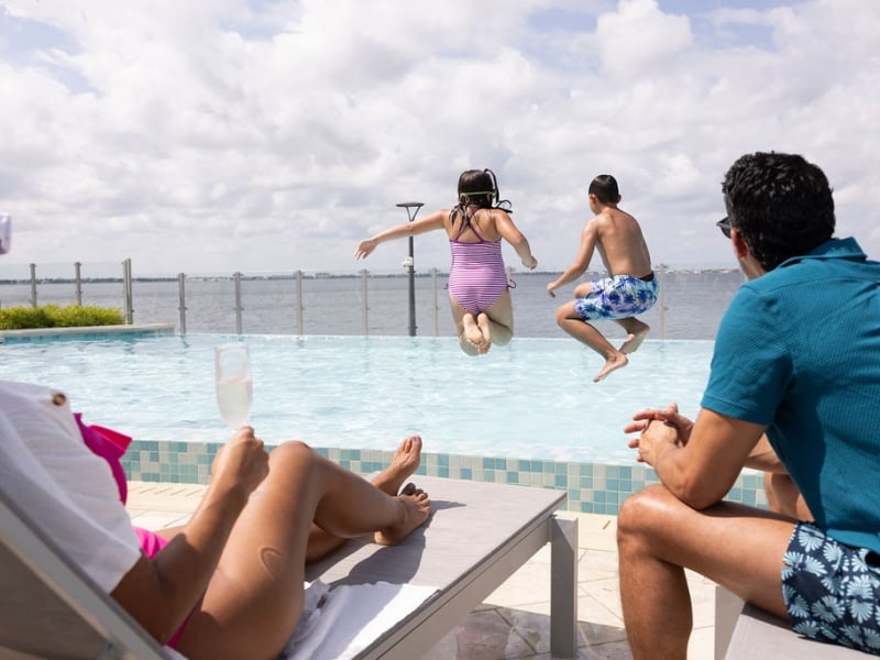 Kids jumping in the pool as parents watch over from sunbeds