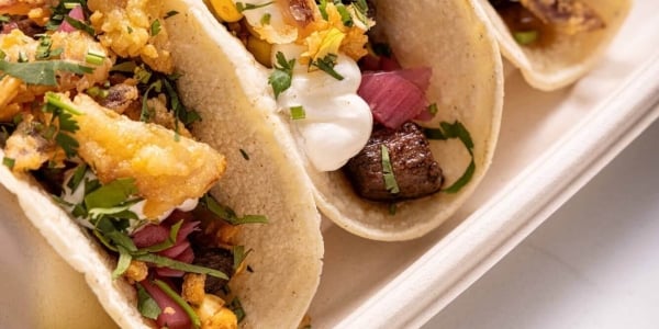 3 tacos served with a slice of lemon on a paper tray