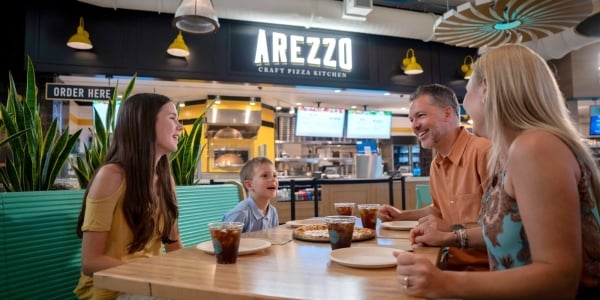 Family enjoying pizza and cola on table outside Arezzo at Harbor Yards Food Hall