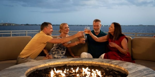 Two couples clinking glasses sitting next to fire pit with charlotte harbor in the background