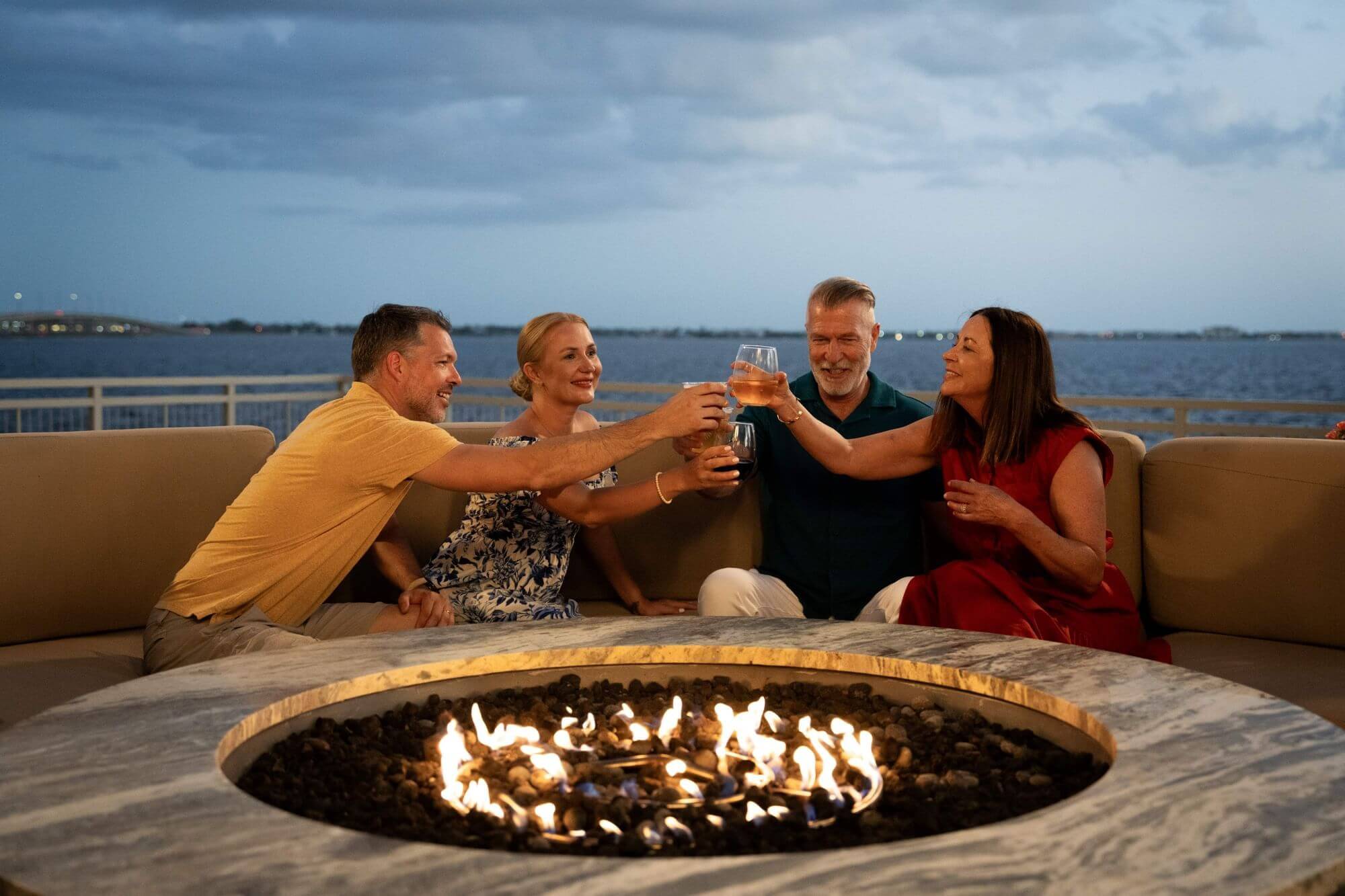 Two couples clinking glasses sitting next to fire pit with charlotte harbor in the background